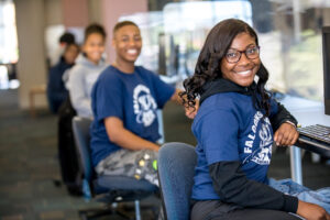 Students sitting at computer desks smiling at camera