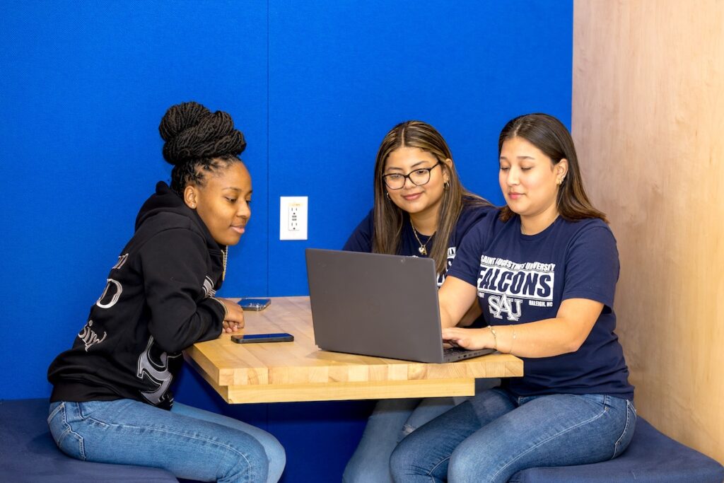 Three students in the student center looking at a laptop.